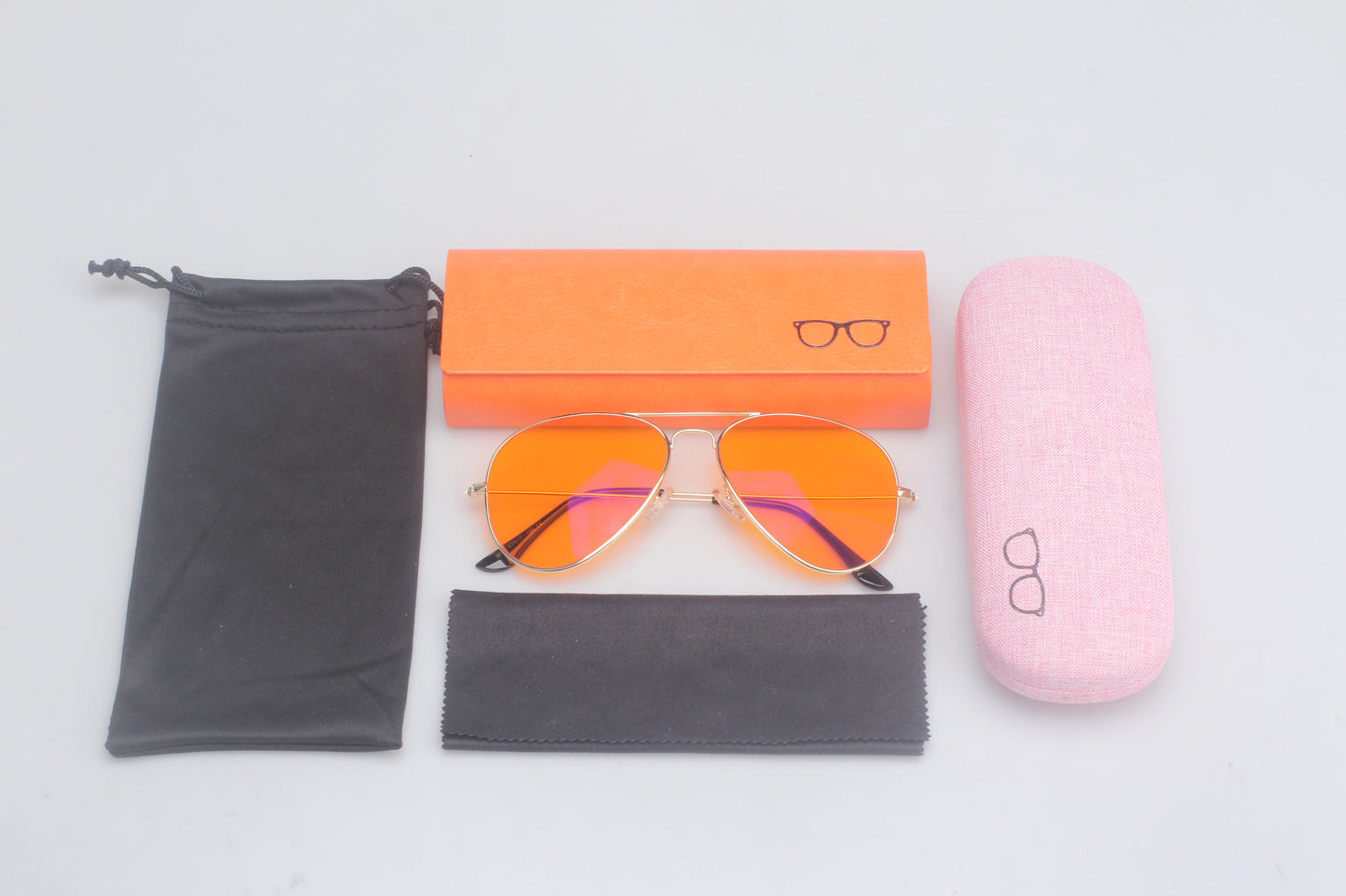 Orange blue light blocking glasses with gold frames on a light gray background, surrounded by a black pouch, orange box, and pink case.