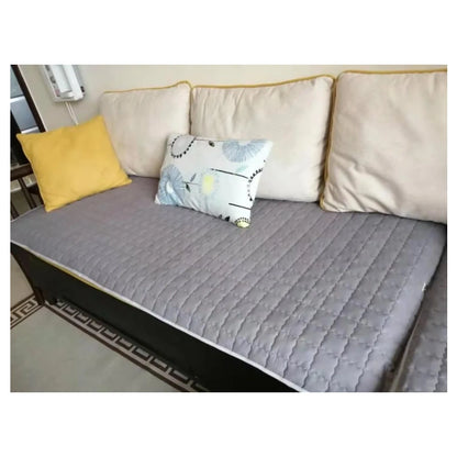 Section of a sofa with a gray quilted Earthing cover, yellow pillow, and patterned white pillow.