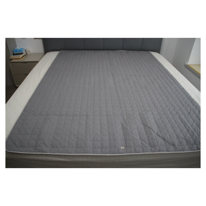 Gray quilted grounding mattress cover on a bed in a room setting.