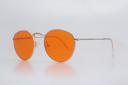 Round orange Blue Light blocking glasses with gold frame on a light gray background