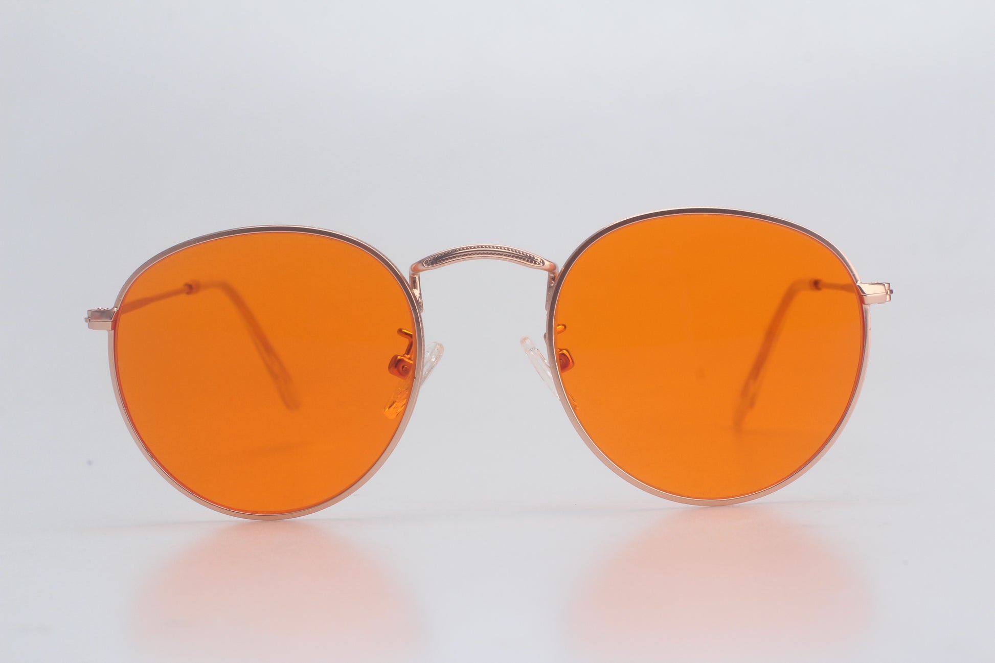 Round orange glasses with gold frame on a light gray background