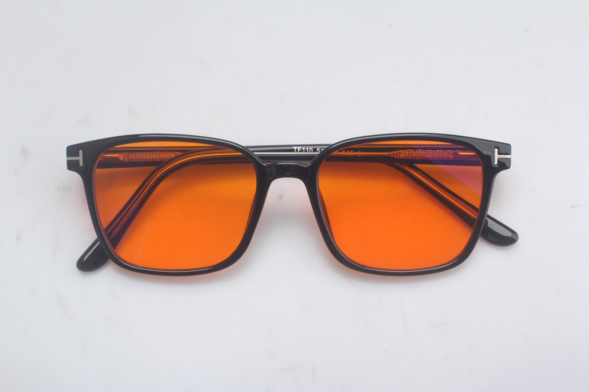 Blue Light blocking glasses with orange lenses and black frames on a light gray background