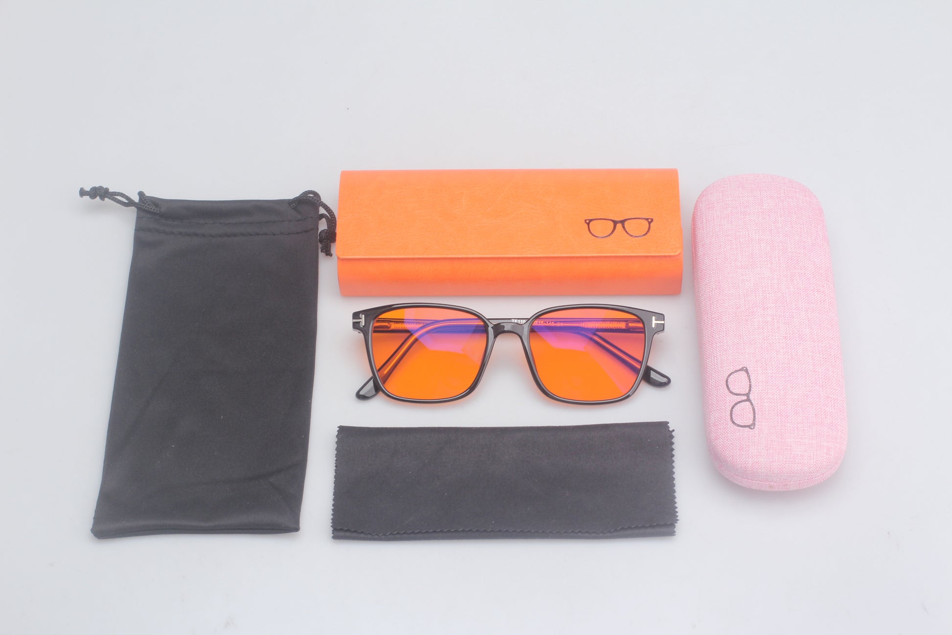 Eyeglasses with orange-tinted lenses, black case, pink case, and cleaning cloth on a light gray background